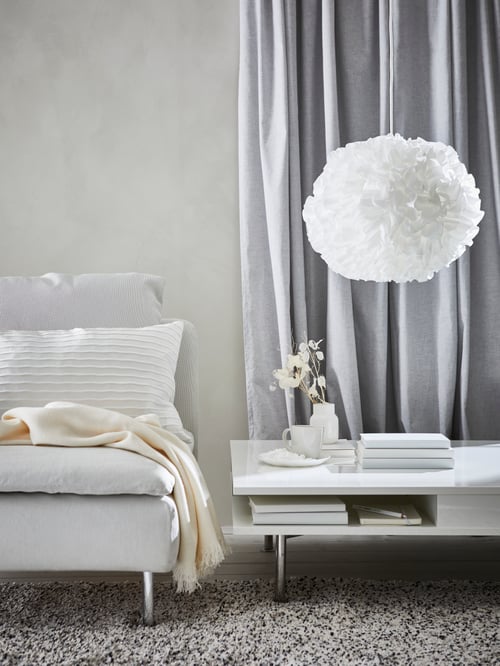 White living room with a VINDKAST pendant lamp over a coffee table next to a chair with throw and cushion and curtain behind.