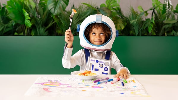 Ein Mädchen in einem Astronautenkostüm isst im IKEA Restaurant ein Kindermenü.