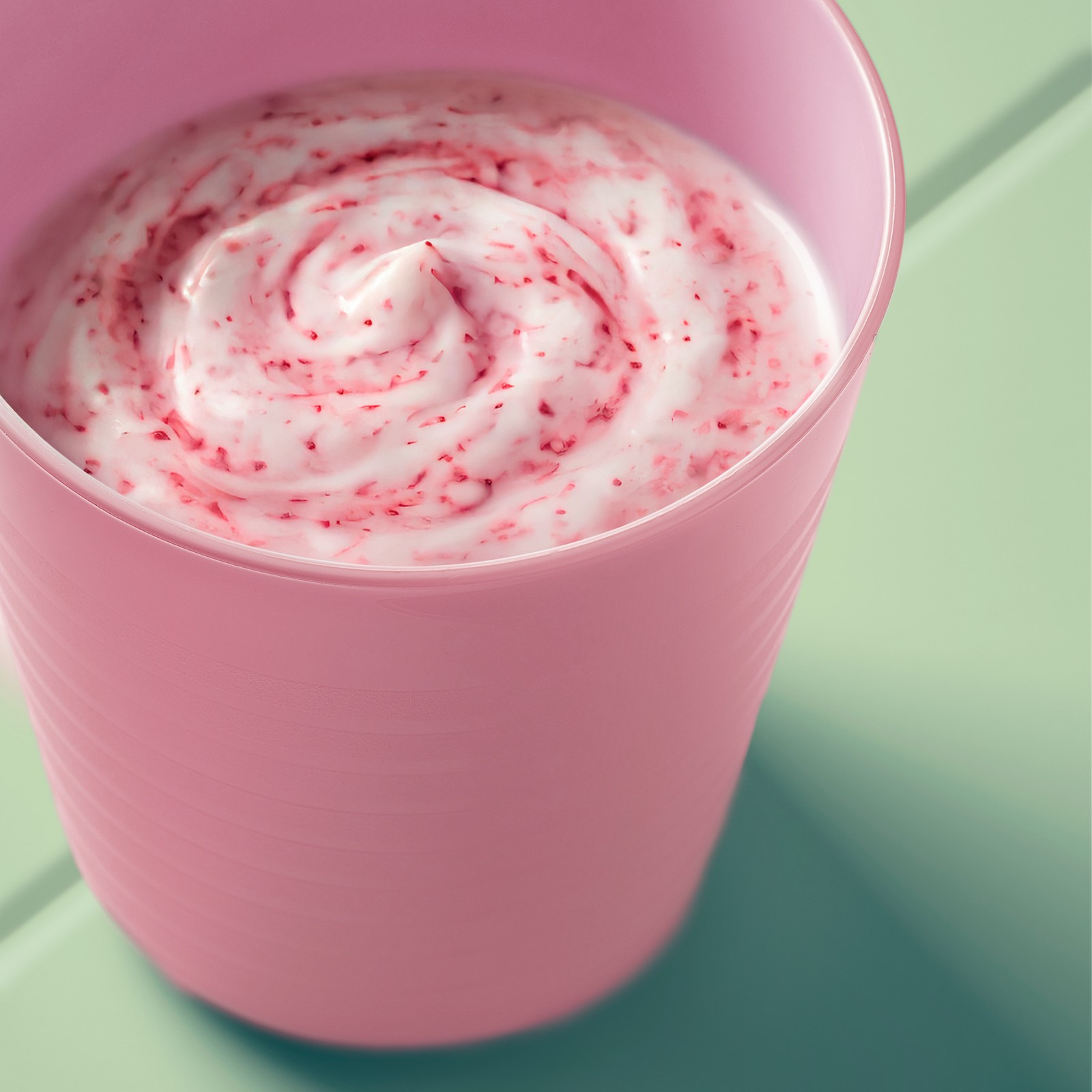 Close-up of a pink kid’s KALAS mug filled with creamy pink smoothe, shown on a light green table outdoors.