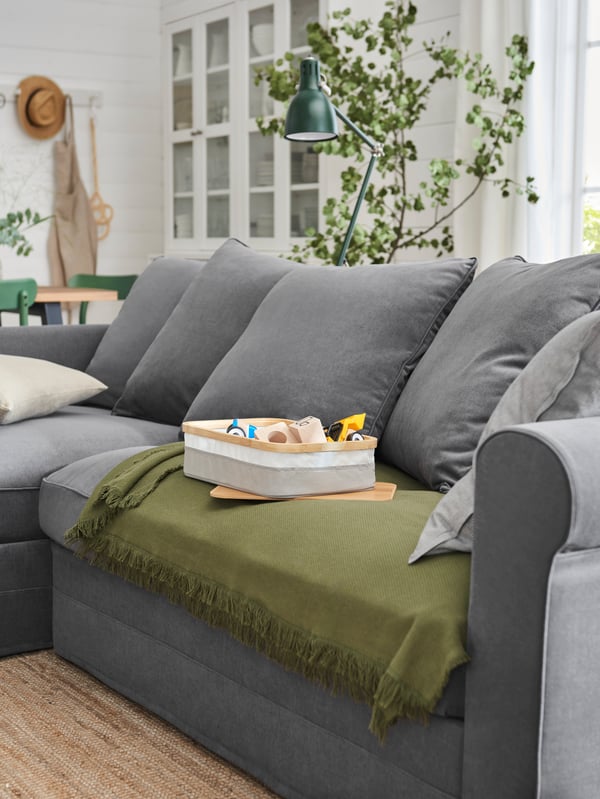 GRÖNLID three-seat sofa with chaise lounge, in Ljungen medium gray, with a dark-green ODDRUN throw.