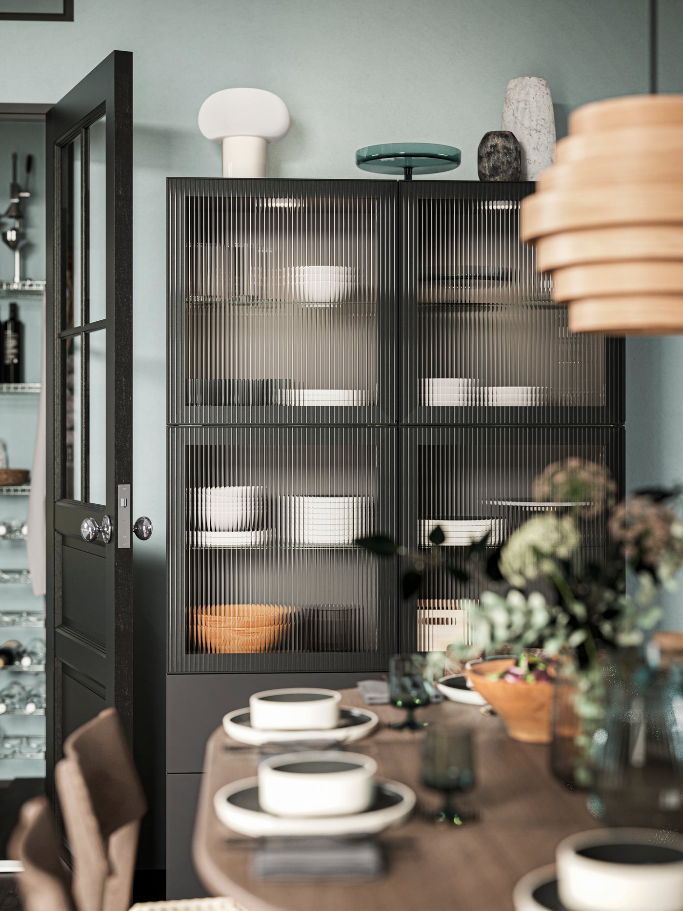 A BESTÅ storage combination with black-brown frame and anthracite/reeded FÄLLSVIK glass door, in a dining room in front of a dining table. 