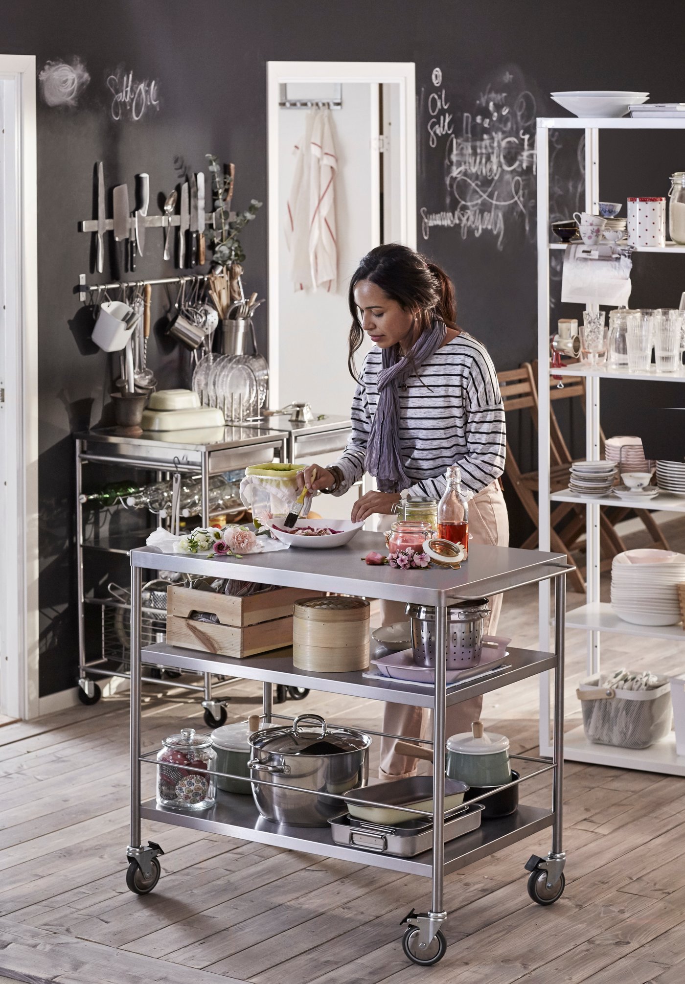 אישה עומדת במטבח ליד עגלת נירוסטה ומבשלת 