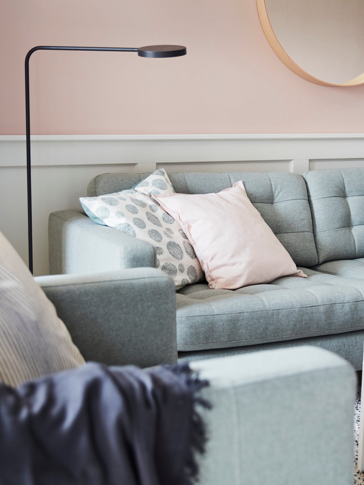 Salón con un sofá de tres plazas con cojines y un espejo en la pared, un sillón y una lámpara de pie.