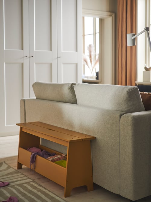 Living room with a beige bench with storage made of wood, placed between a 2-seat sofa bed and a rug low pile.