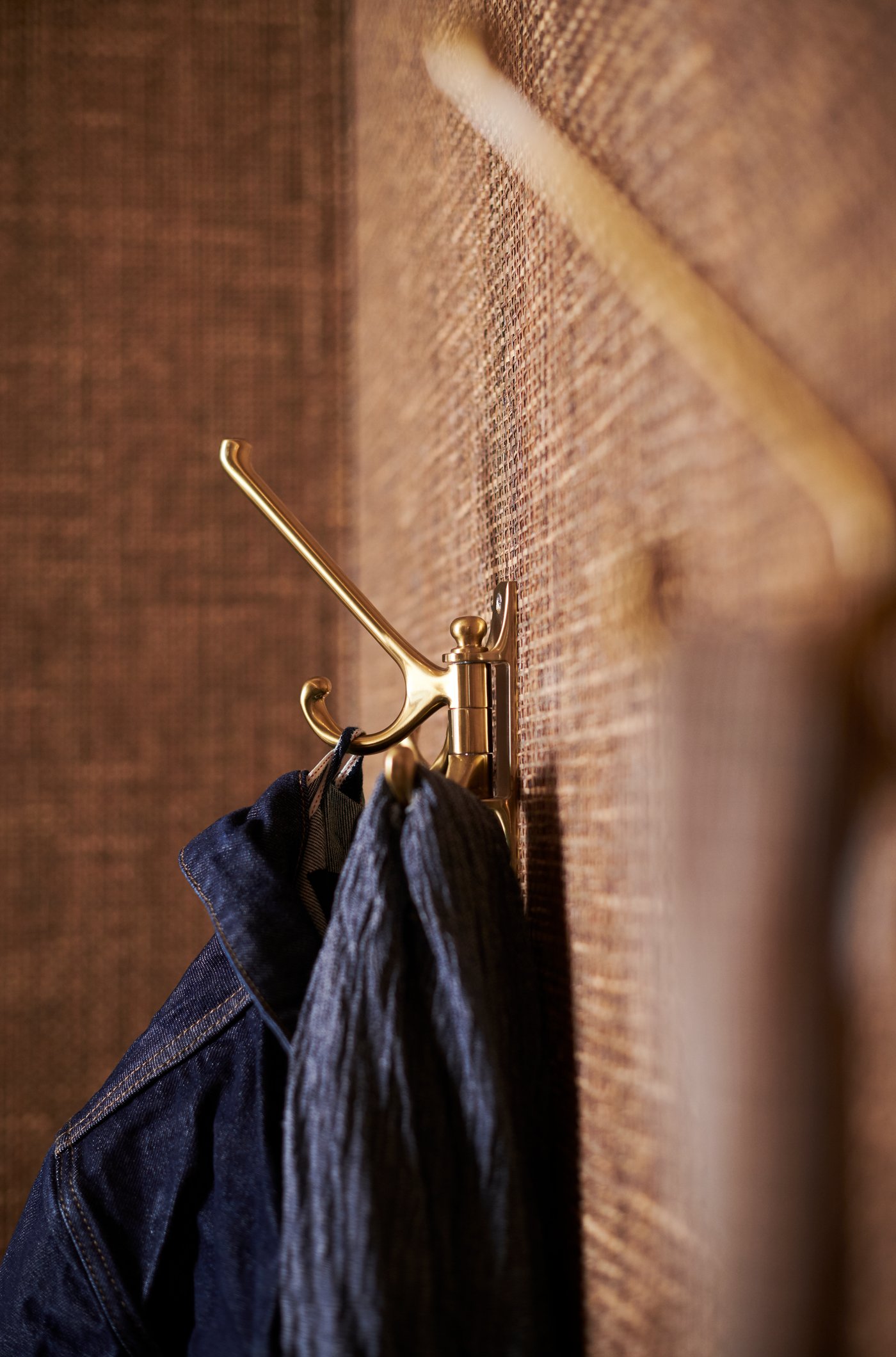 A wall‑mounted metal hook with garments hanging from it, photographed up close against a textured wall.