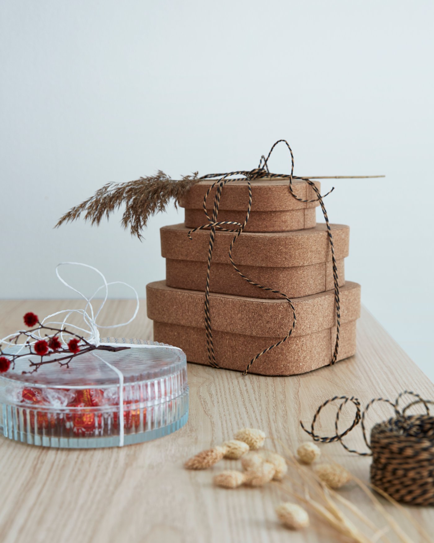 Drei SAMMANHANG Schachteln aus Kork, mit Schnur zusammengebunden. Danaben ist ein SAMMANHANG Glasbehälter mit Deckel und Süssigkeiten darin zu sehen.