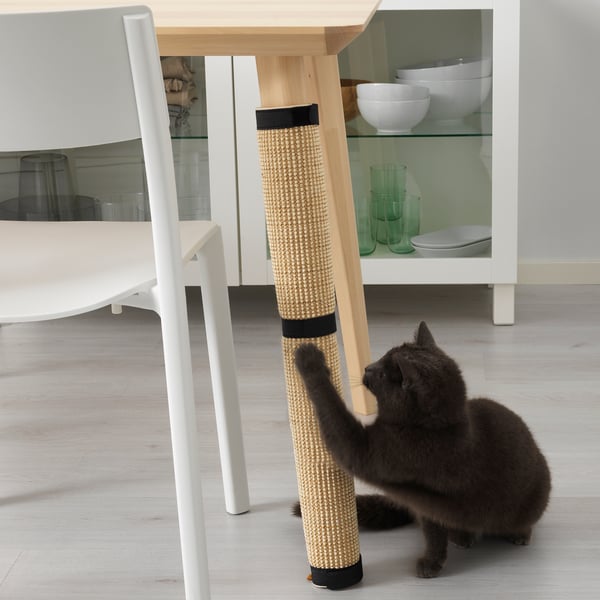 A cat scratching its claws on a UTSÅDD scratch mat in natural materials, wrapped around a table leg, and a chair beside.