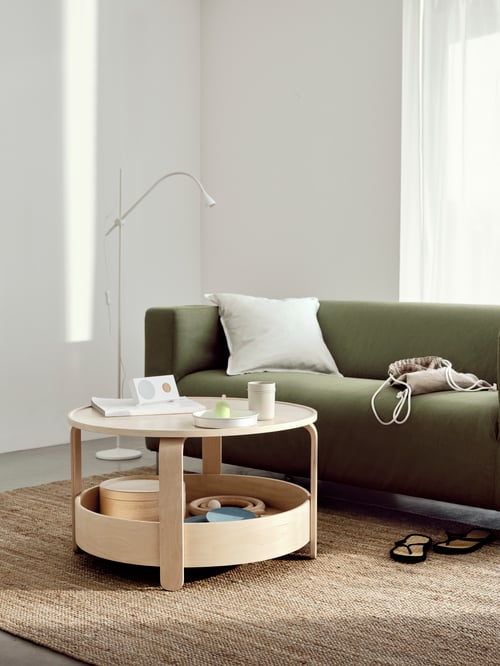 Salon avec une table basse ronde, un lampadaire à DEL, un haut-parleur portable Bluetooth, un canapé deux places, une housse, un tapis.