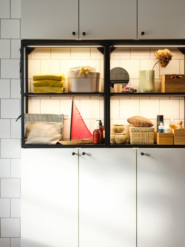 An anthracite-and-white ENHET wall storage combination placed against a white-tiled wall, holding bathroom accessories.
