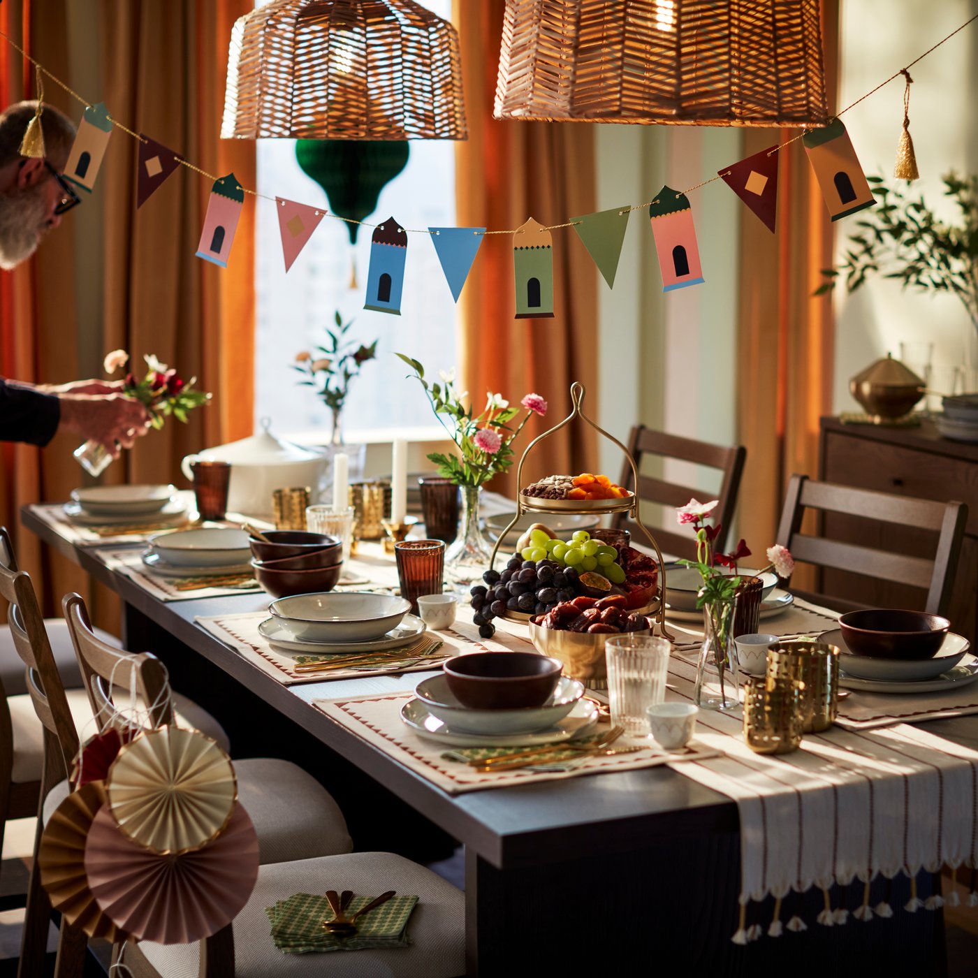 A beautifully set dining table adorned with a gold-coloured GOKVÄLLÅ two-tier serving stand displaying treats and fruits