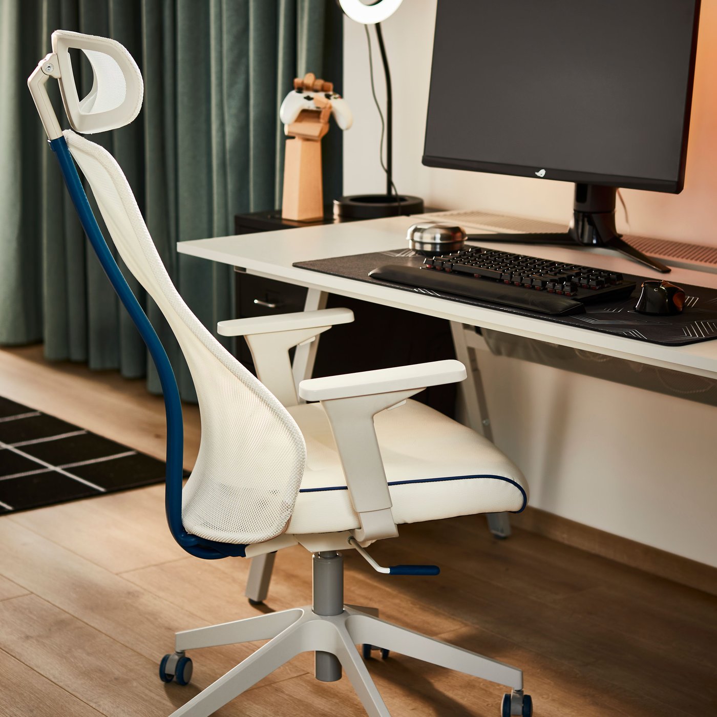 كرسي لعب Bomstad / MATCHSPEL لونه أبيض موضوع على أرضية خشبية مع ستائر HANNALENA لتعتيم الغرفة باللونين الأخضر والأزرق في الخلفية.