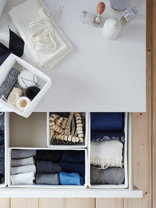 SKUBB boxes sit inside the open drawer of a chest of drawers. One SKUBB box sits on top along with other items.