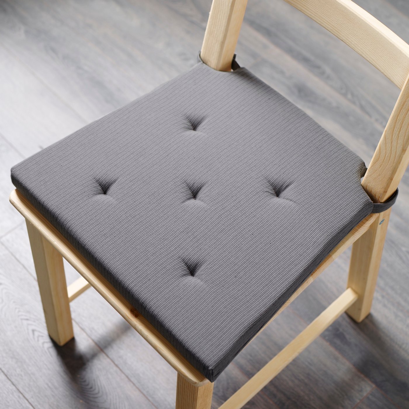 A wooden dining chair with a grey JUSTINA chair pad.
