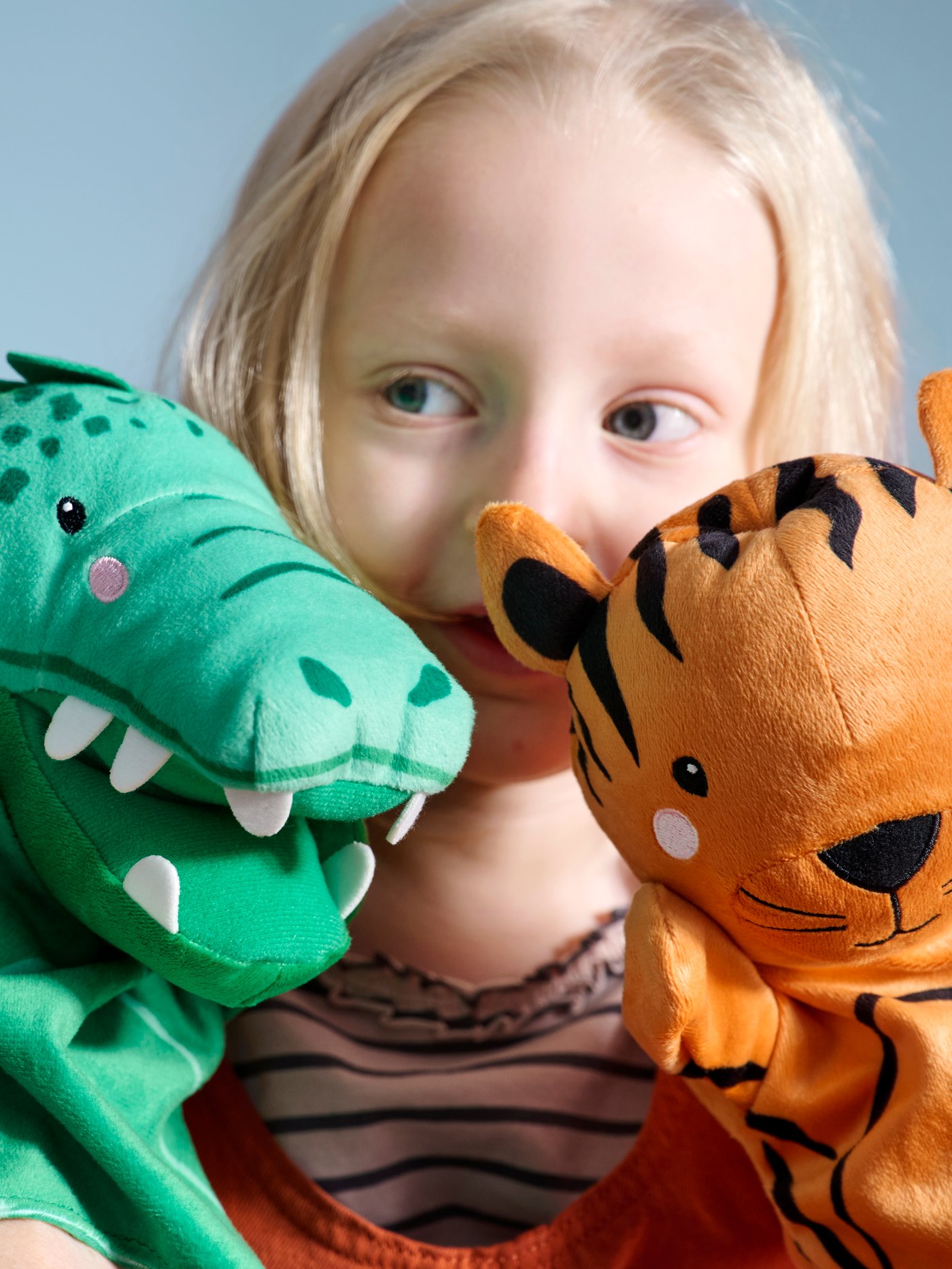 Close-up of a little child playing with hand puppets, a bright green crocodile to the left and an orange tiger to the right.