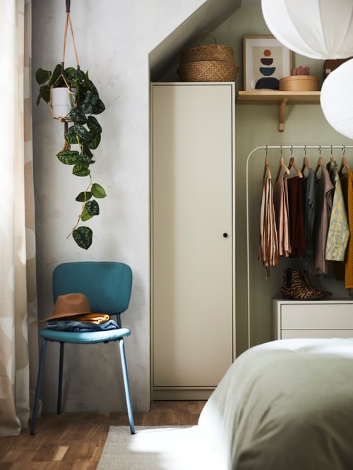 Baby and children room with a beige wardrobe made of wood, placed next to a white cabinet with 2 drawers and a clothes rack.