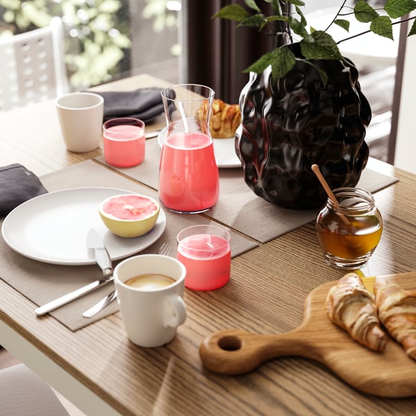 A brunch table setting for two, with coffee, juice, fresh fruit and croissants, is placed on an ÅLHULT extendable table.