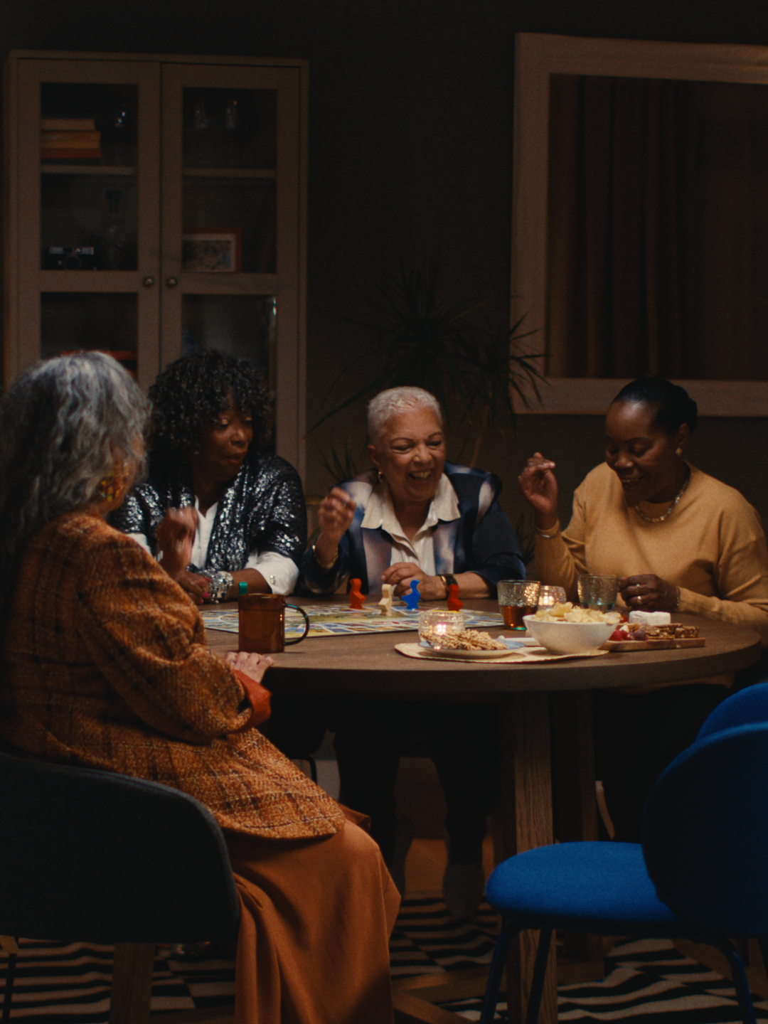 Mensen zitten lachend aan een tafel en hebben drinkglazen en spelletjes voor zich op tafel staan.