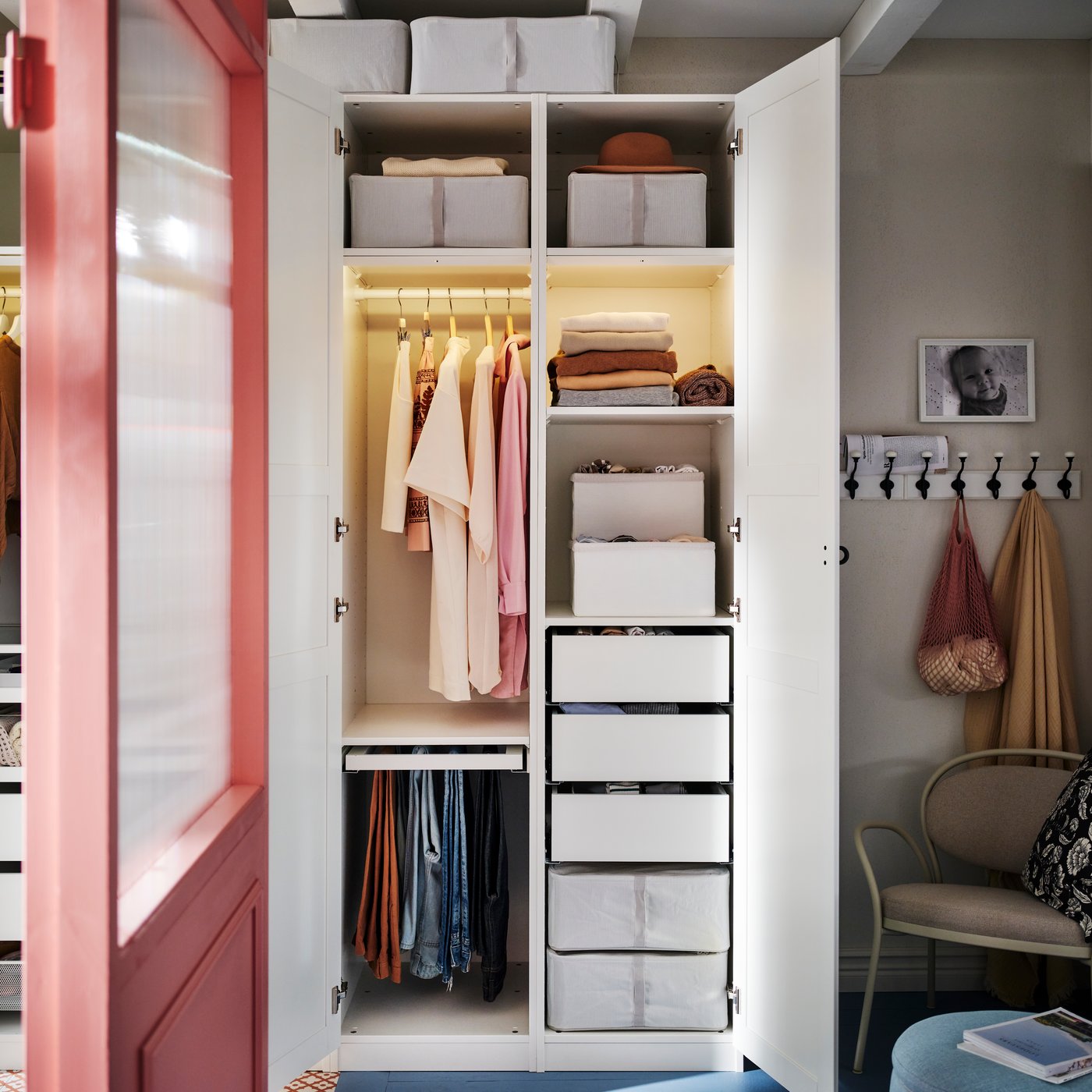 Een witte PAX/TYSSEDAL-kledingkast met open deuren waarin georganiseerde kleding te zien is en twee HEMMAFIXARE-boxen op de bovenste planken.