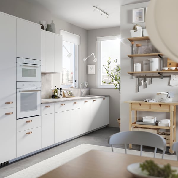 Simple white Scandinavian kitchen with grey dining chairs and blonde wood storage including butcher’s kitchen trolley with drawers.