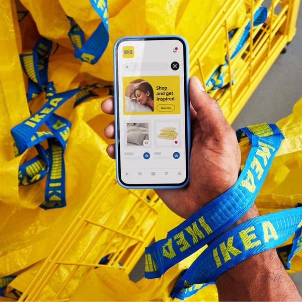 mobile phone in one hand with the IKEA App and yellow bags