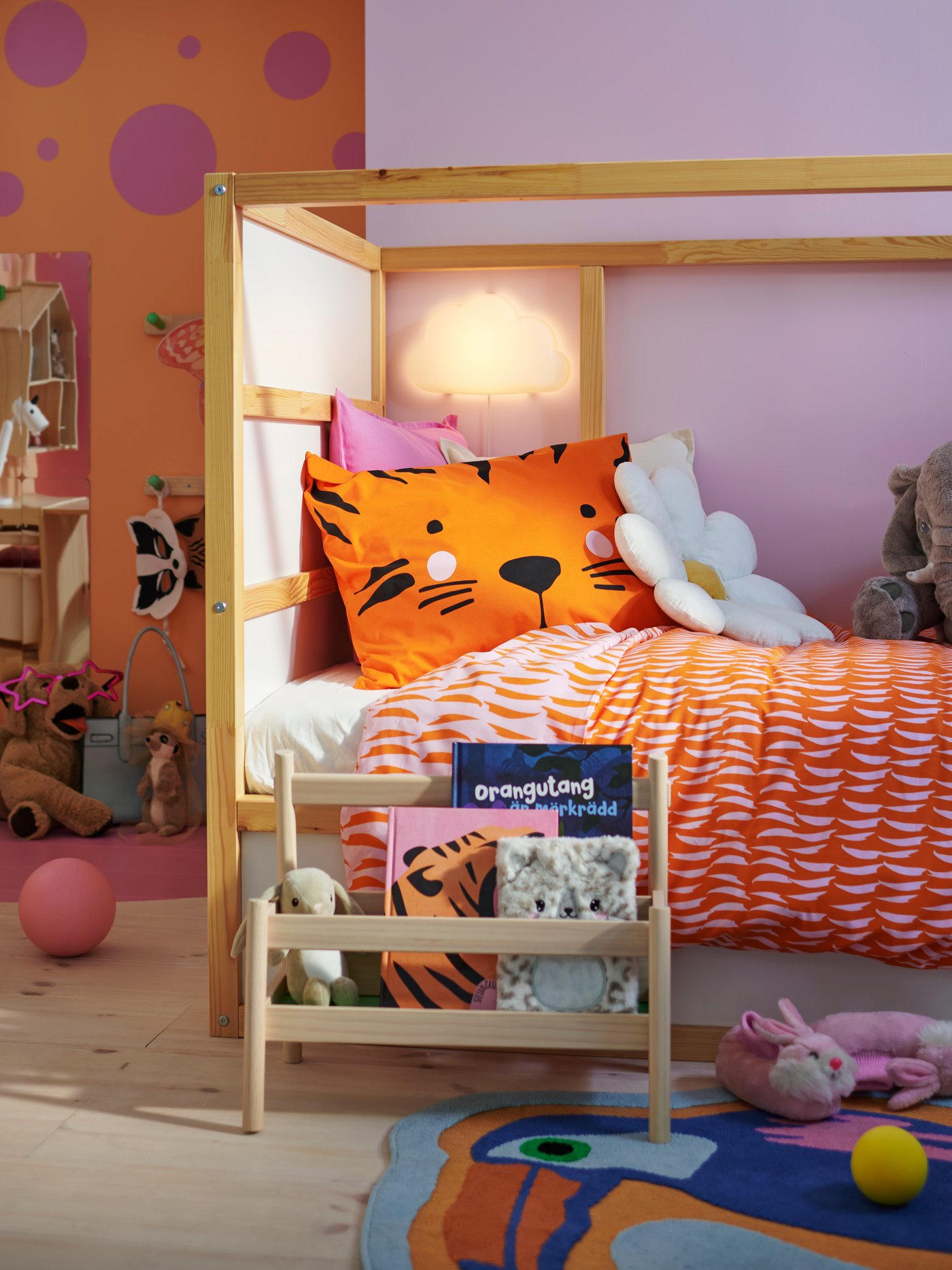 En KURA vändbar säng i ett färgstarkt barnrum, med mjuka gosedjur på sängen och en FLISAT bokhylla framför.