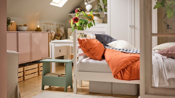 A rustic-style bedroom contains a white HAUGA extendable table by a white TARVA bed covered in red-brown ÄNGSLILJA bed linen. 