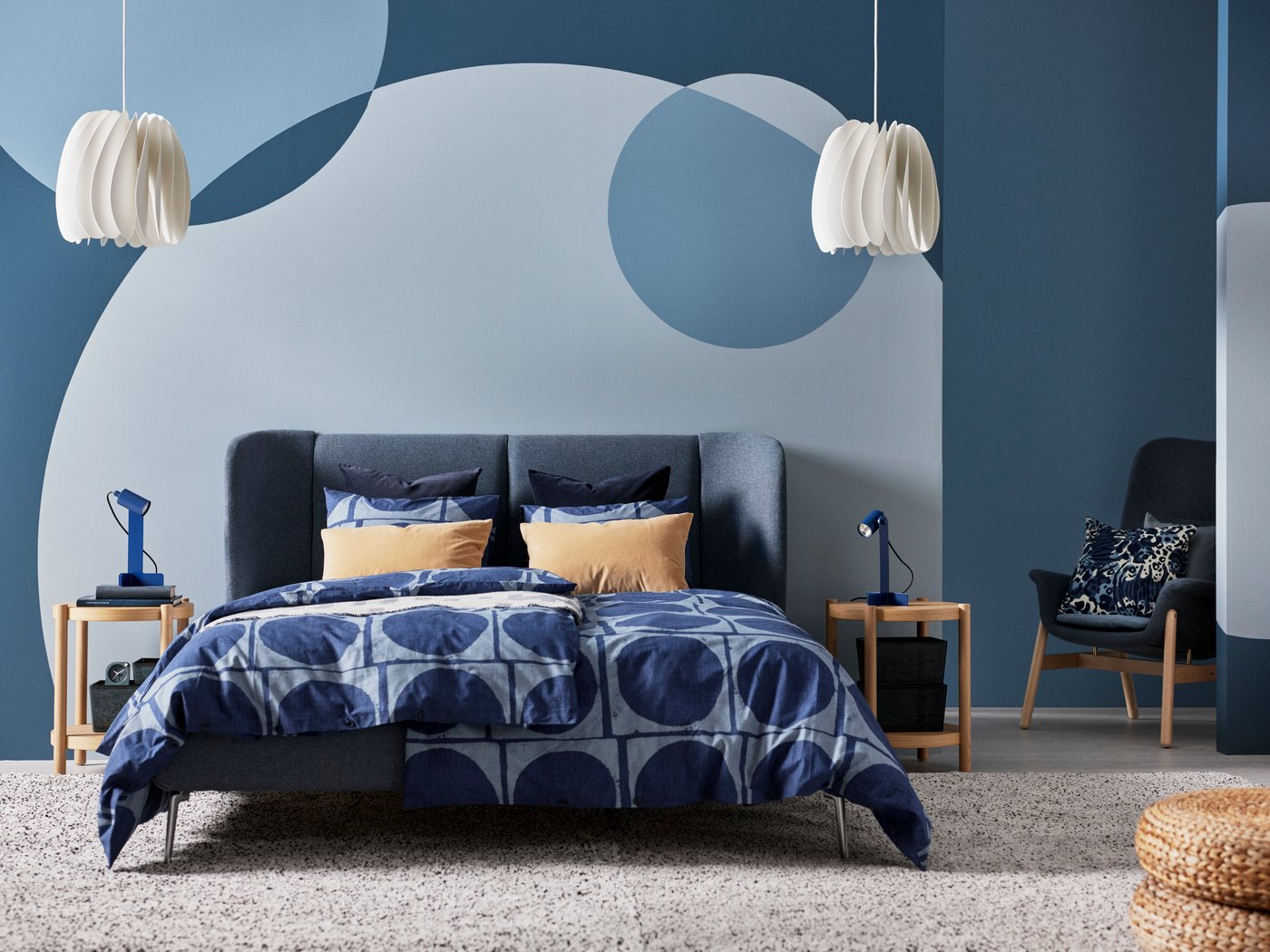 Et blåt soveværelse med en polstret blå dobbeltseng med dynebetræk og gule hovedpuder.