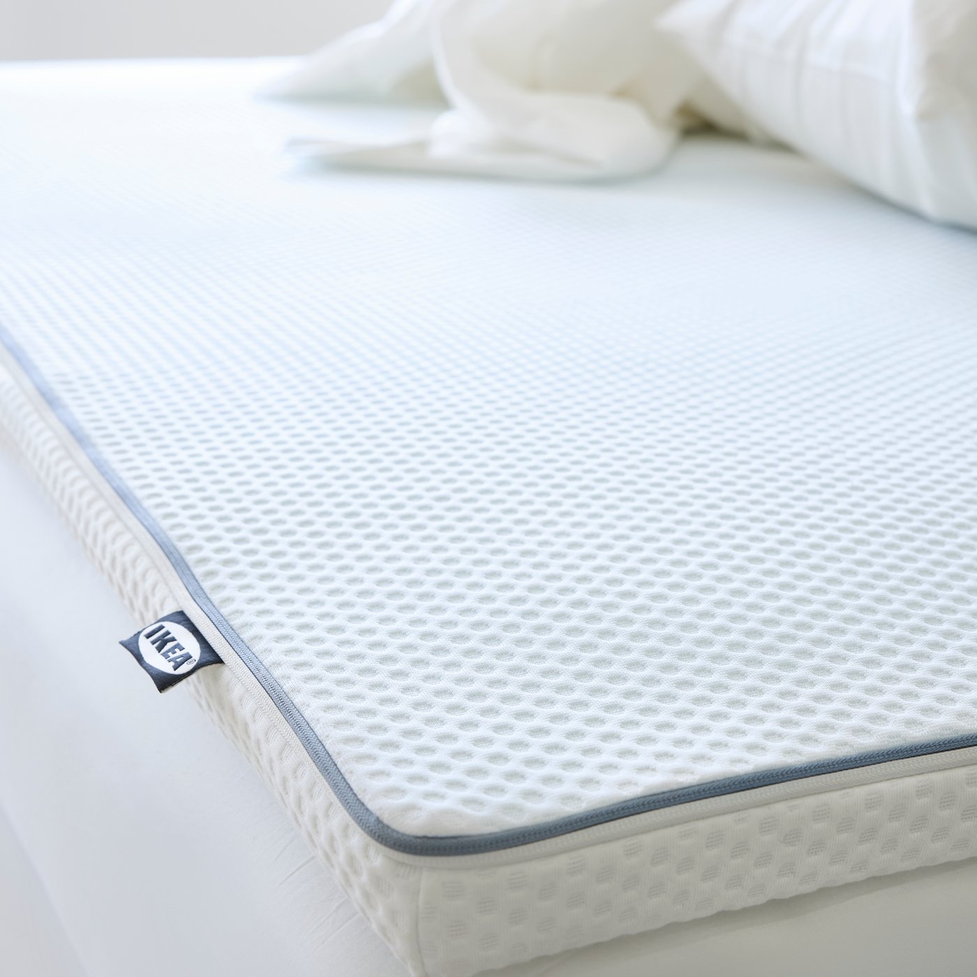 A NISSEHOLM mattress pad in a bright white space. There is a sheets crumbled up at the end.