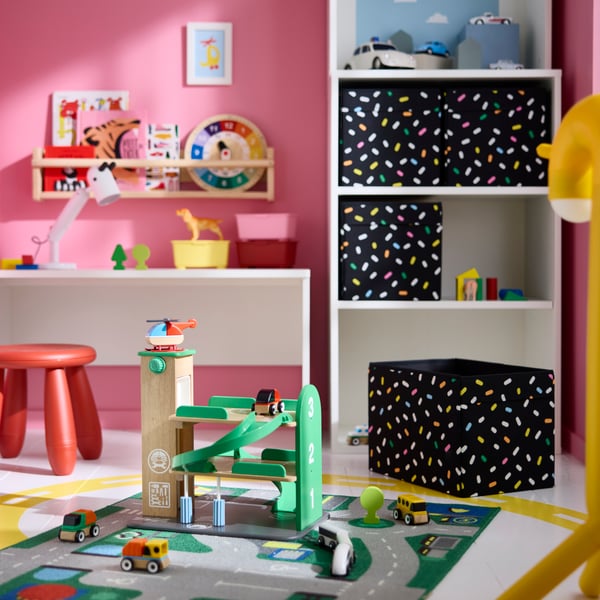 Eine LILLABO-Garage mit Auto und Hubschrauber auf einer Spielmatte in einem Kinderzimmer mit bunten Regalen und Aufbewahrungsmöbeln.