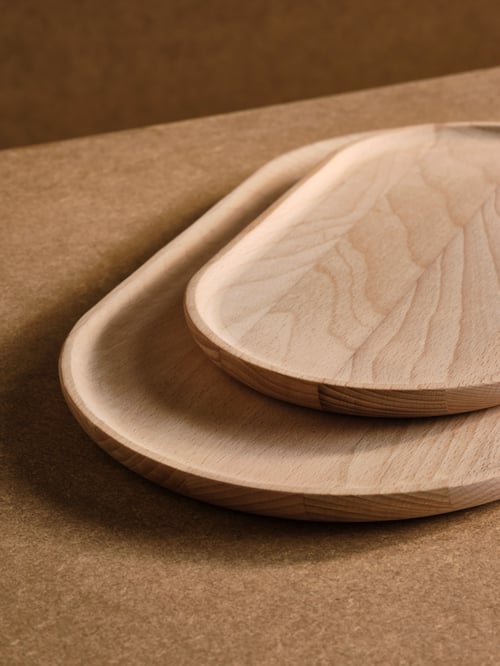 A set of two SMÖRLING serving trays featuring a beech effect are stacked on a beige surface, with the small tray on top.