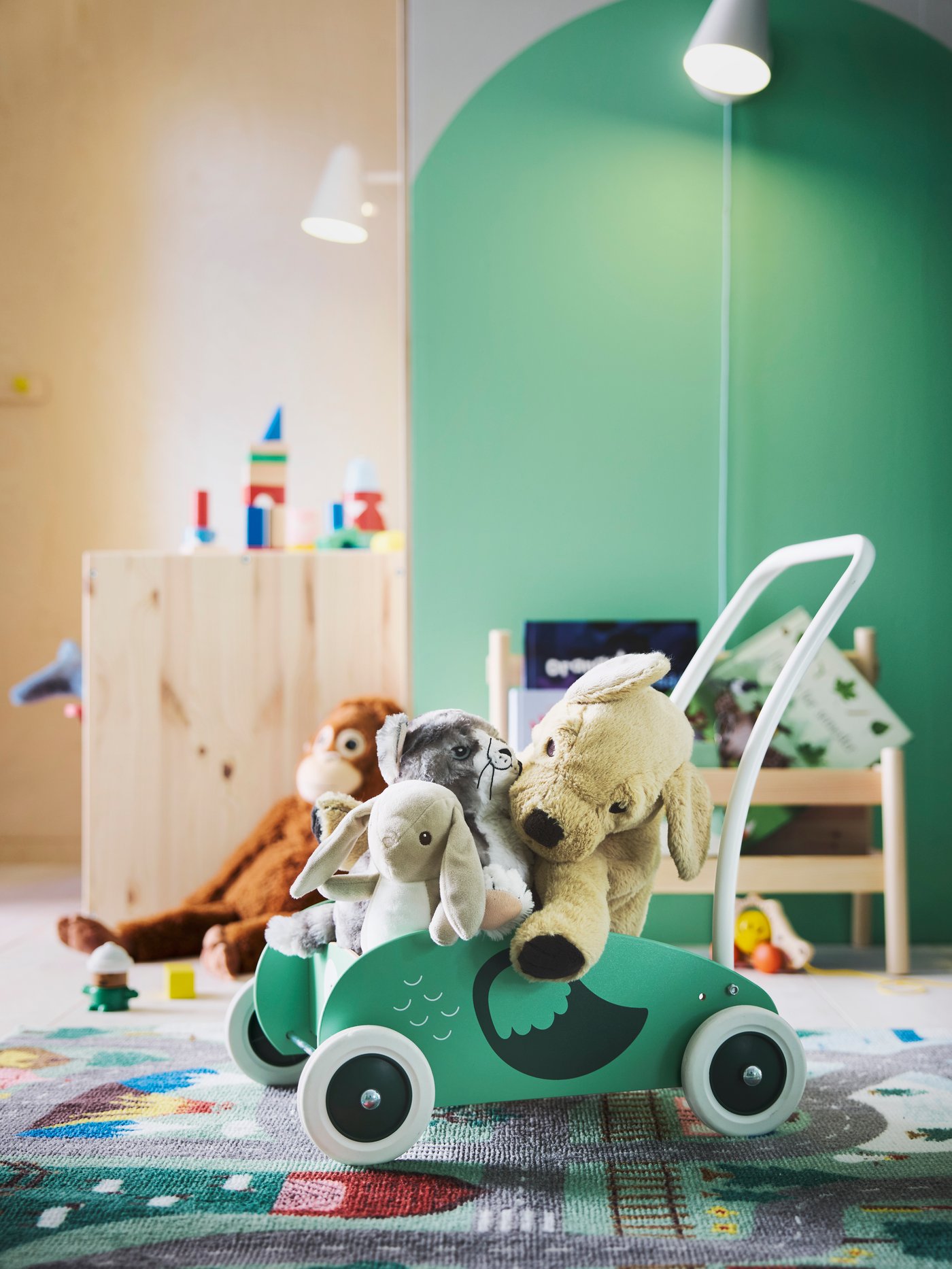 En UPPSTÅ baby gåvogn fyldt med tøjdyr foran en grøn væg og et VALLABY gulvtæppe under det.