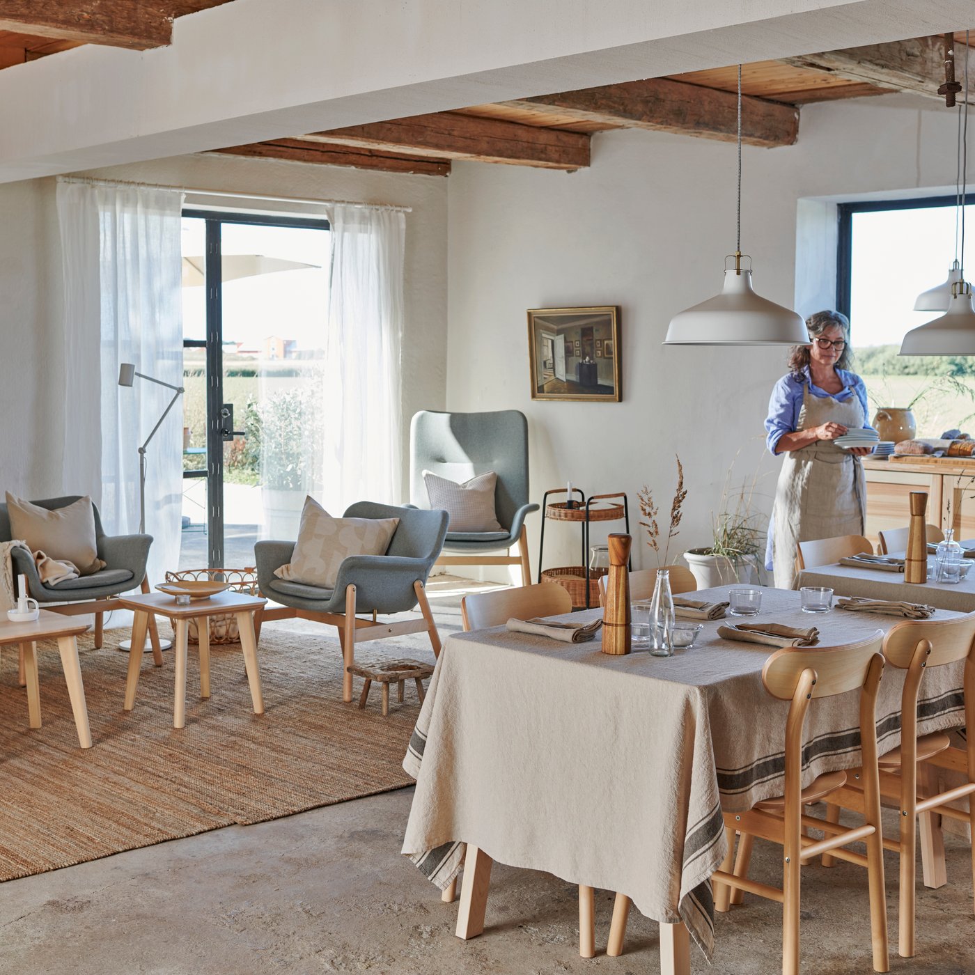 A large and bright living and dining space in traditional style with wooden beams in the ceiling and concrete floors.