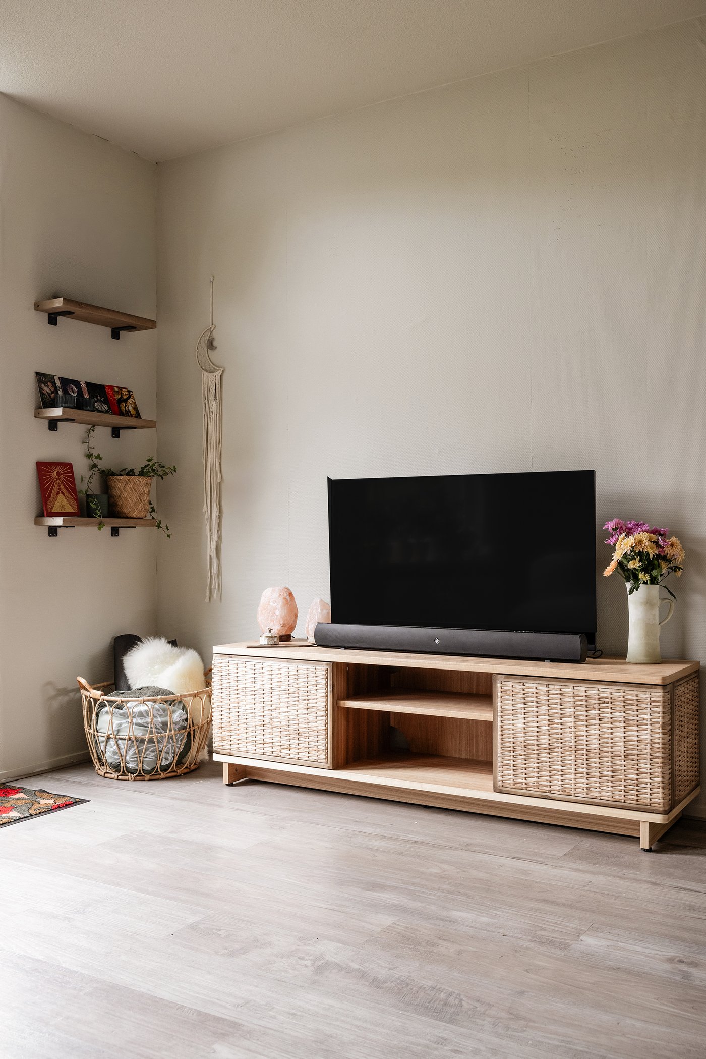 Hoek van een woonkamer met tv-meubel waarop een tv staat. Aan de muur hangen drie plankjes met accessoires.