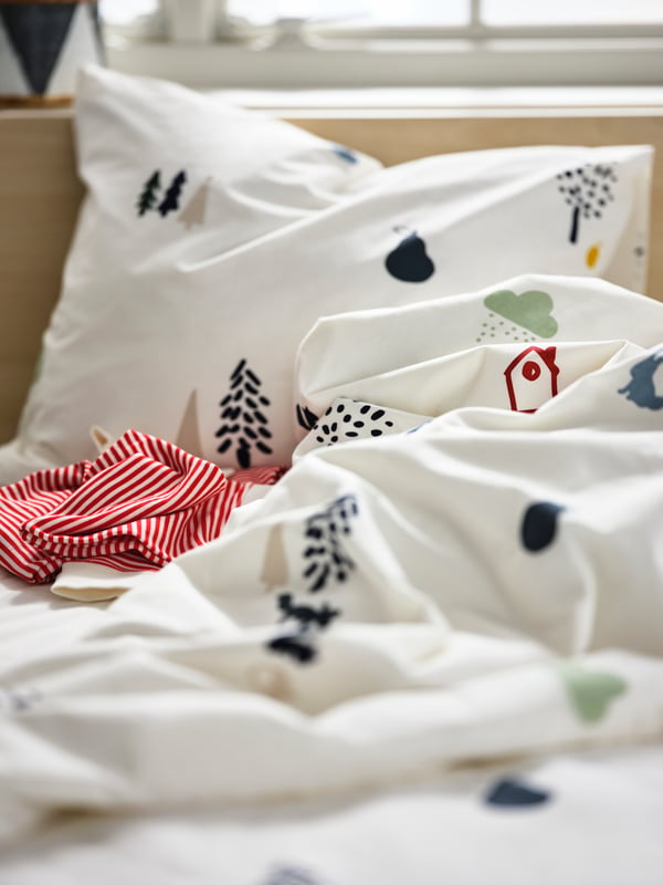 A striped pyjama piece left on a ruffled children’s bed made with white-and-forest-animal-patterned BARNDRÖM bed linen.