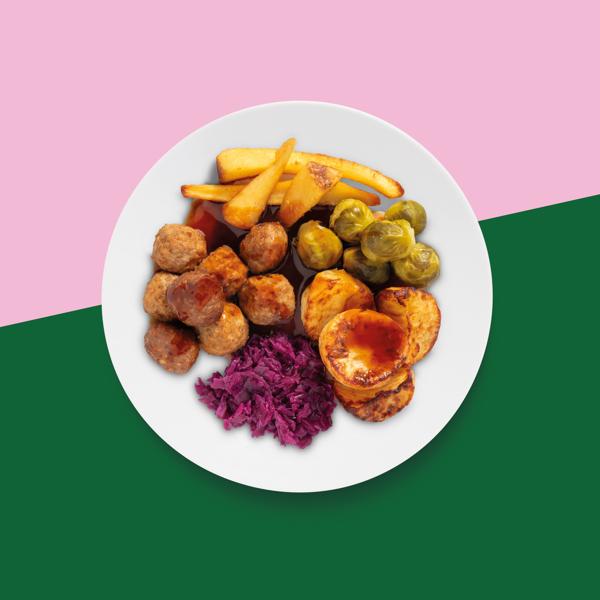 A plate of festive meatball served with roast potatoes, sprouts, parsnips, red cabbage & gravy, on a green and pink background.