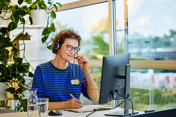 In an office with big windows and live plants, a specialist adviser receives a remote sales call.