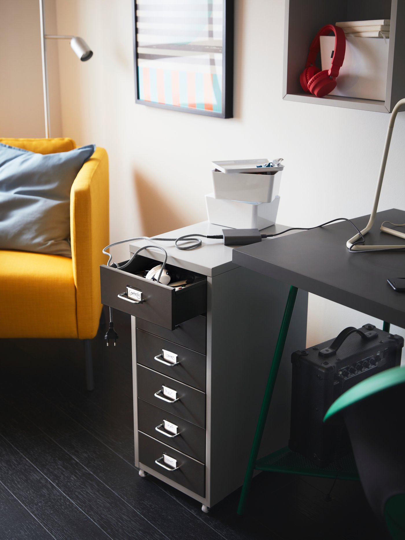 A HELMER dark grey and light grey drawer unit on castors with the top drawer open, between a desk and a yellow armchair.