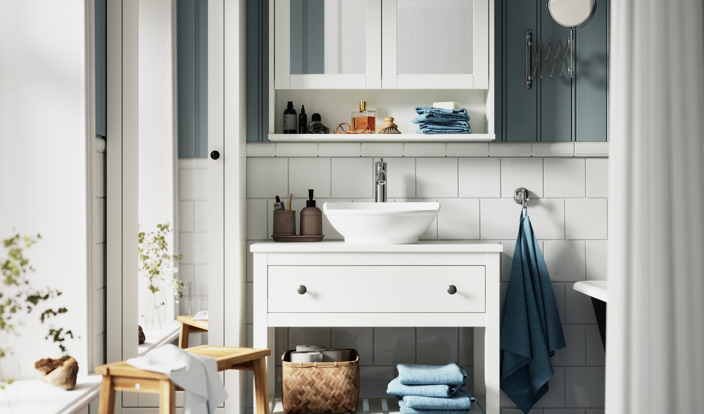 Un mobile per lavabo HEMNES bianco, con un lavabo da appoggio VÄSTERSJÖN bianco è posizionato sotto un mobile a specchio HEMNES.