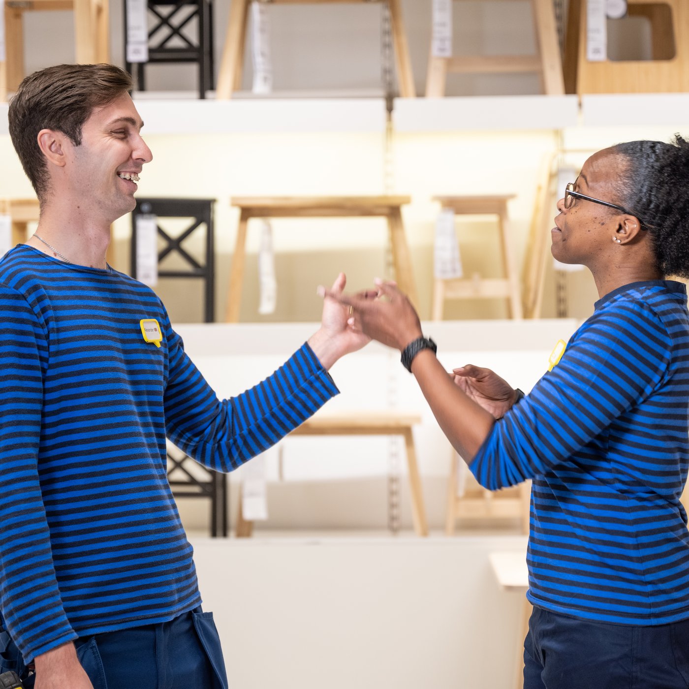 Kaksi sinipaitaista IKEA-työntekijää keskustelevat tavaratalon tuoliosastolla.