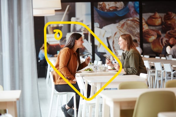 To personer sidder overfor hinanden i en IKEA restaurant og spiser et måltid.
