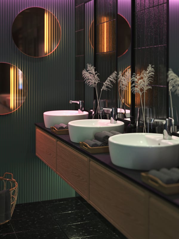 A stylish restroom with dark green walls, round VARMBLIXT mirrors LED wall mirrors, and decorative grass in BERÄKNA vases.
