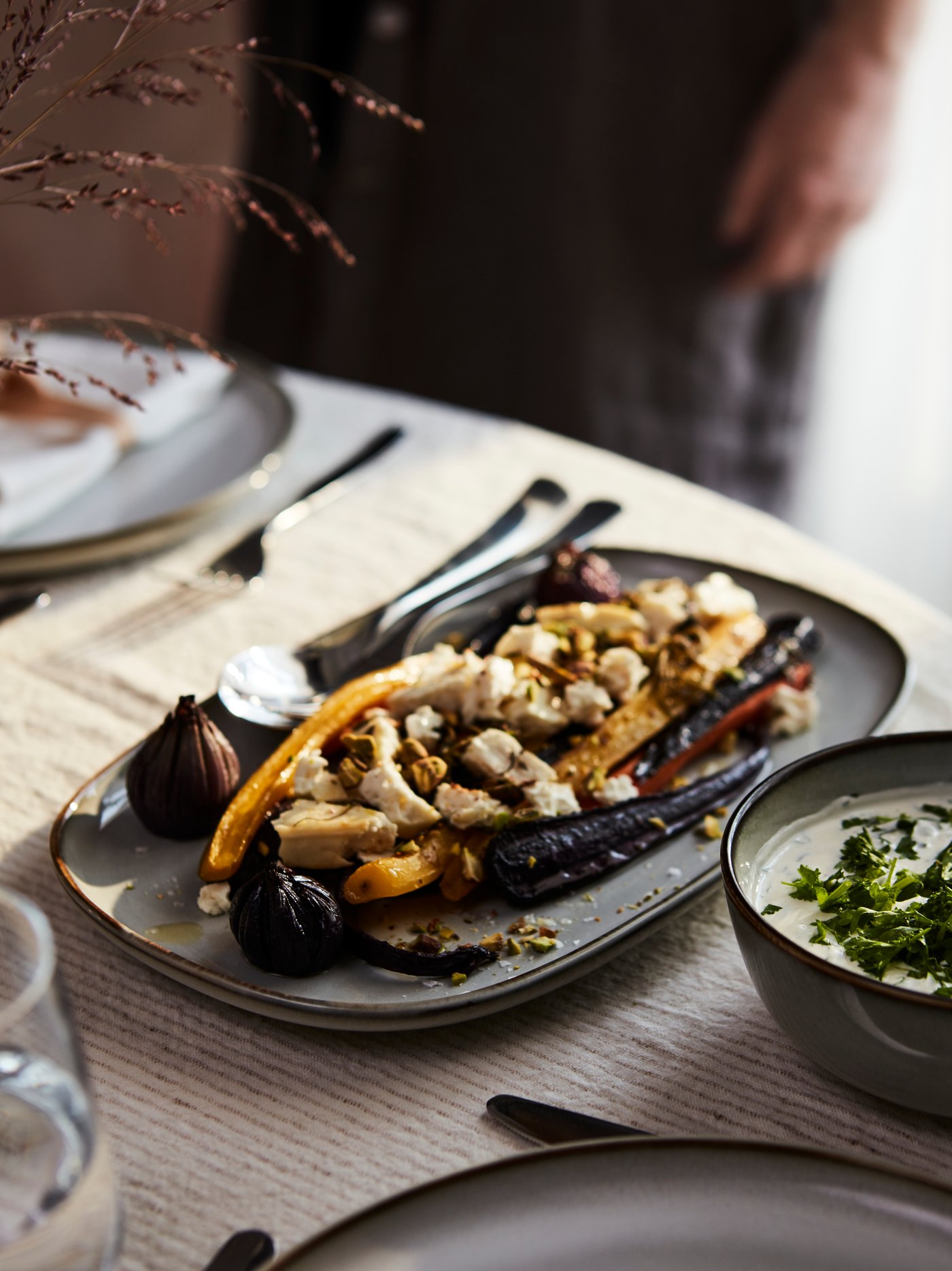 Roasted vegetables on a grey GLADELIG plate and a grey GLADELIG bowl full of soup are on a table set for an autumn feast.