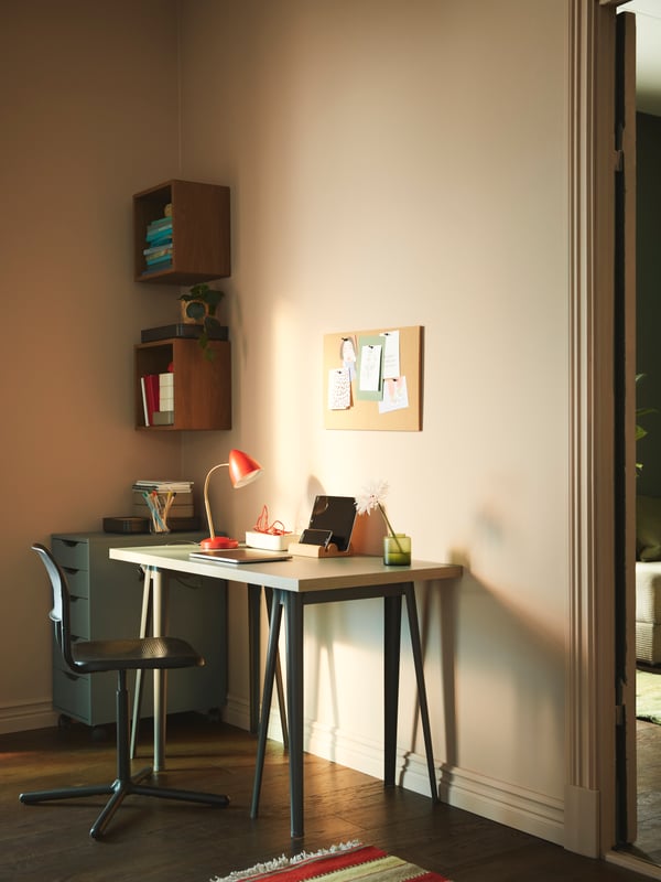 Un escritorio IKEA apoyado en una pared y frente a él una silla SMÄLLEN. En la pared hay una pizarra de corcho con notas.