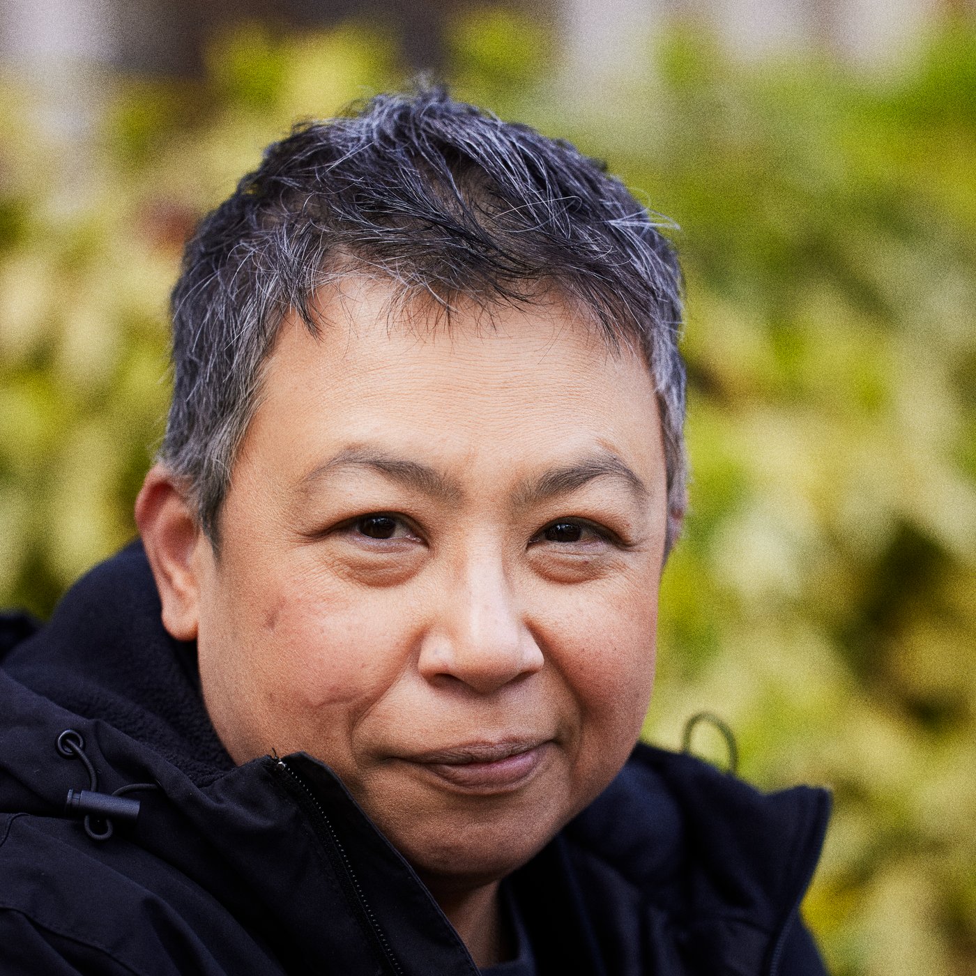 Face portrait of Nancy outside with blurred greenery in the background.