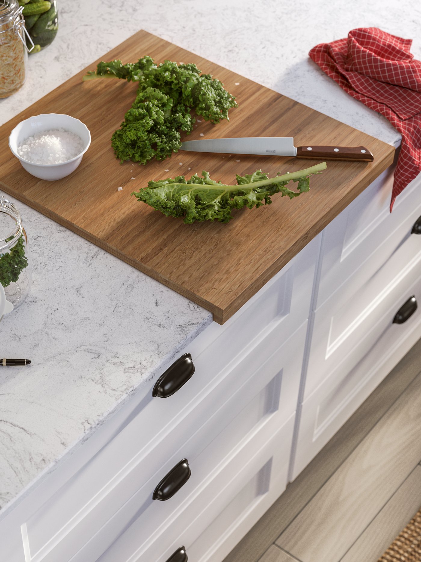 Une planche à découper avec du chou frisé frais et un couteau sur un plan de travail en quartz, à côté d'une bouteille et de bocaux.