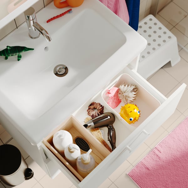 An UPPDATERA storage box, placed inside an open drawer in a bathroom, holding a hair dryer, brush and toiletries.
