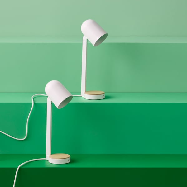 Two slim and lightweight white ENSMÄRKE desk lamps sit on different levels of a green, stairs-like structure.
