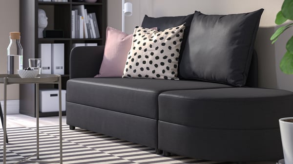 Mörk LINDÅKRA bäddsoffa med raka linjer och dekorationskuddar i stilren inredning.