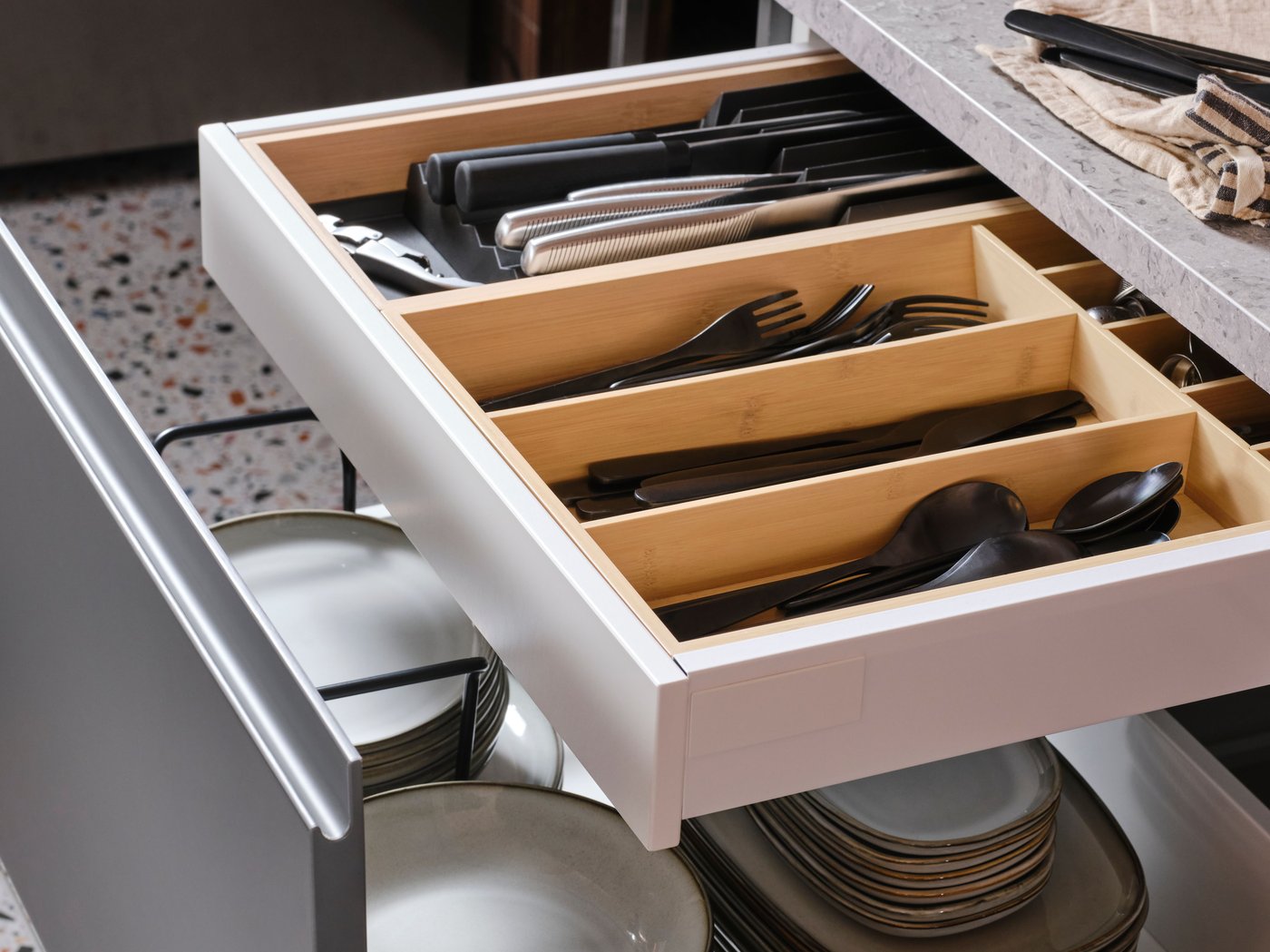 En åben køkkenskuffe med tallerkener og en anden køkkenskuffe indeni med en lys UPPDATERA bestik-/knivholder i bambus indeni.