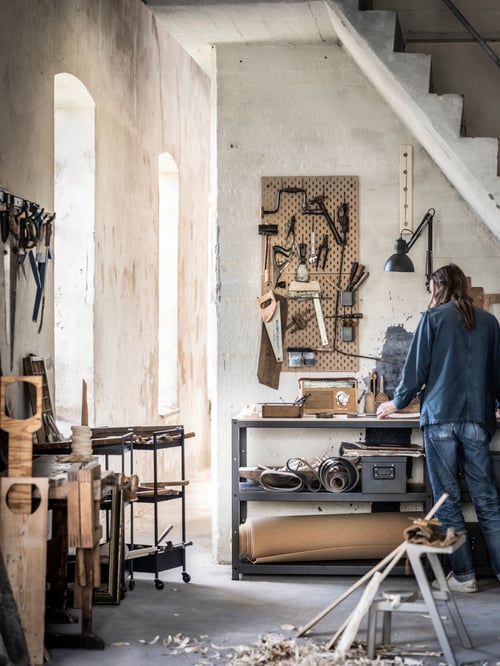 A person is at a black work bench with a work lamp and a pegboard mounted on the wall, and a trolley to the side.